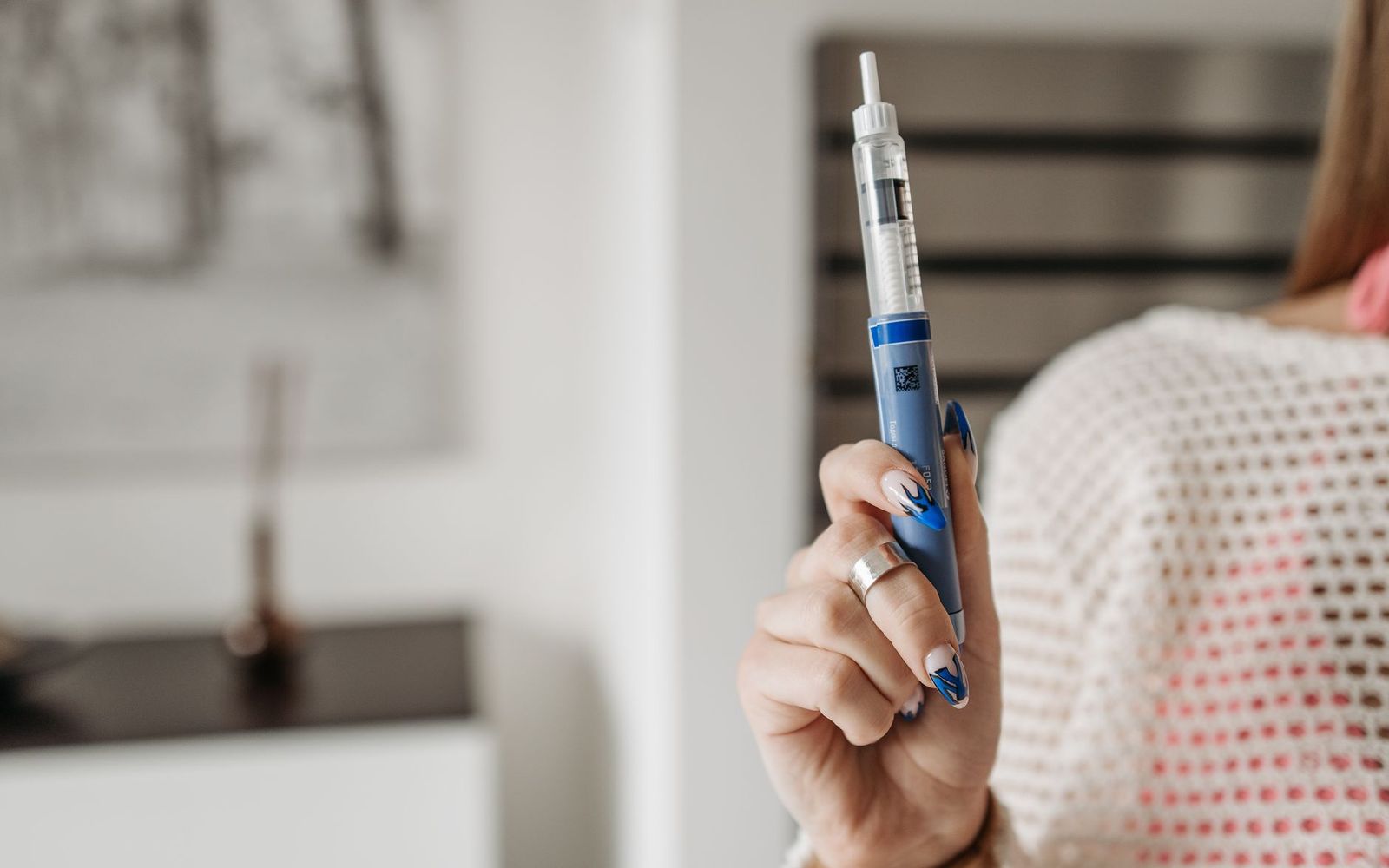 A woman's hand holding a blue injection pen in a bright room.