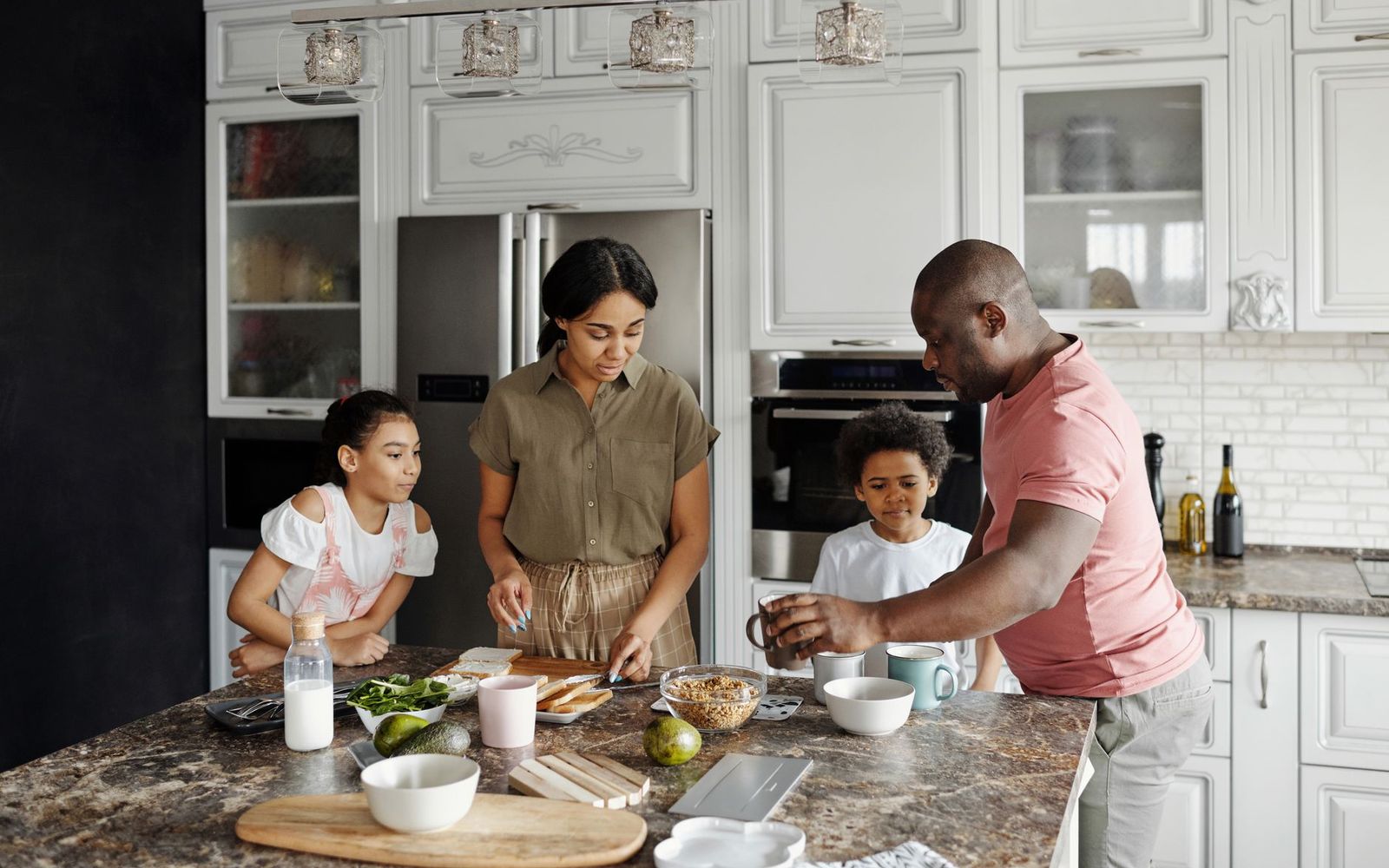 A family of four preparing a meal together around a kitchen island.