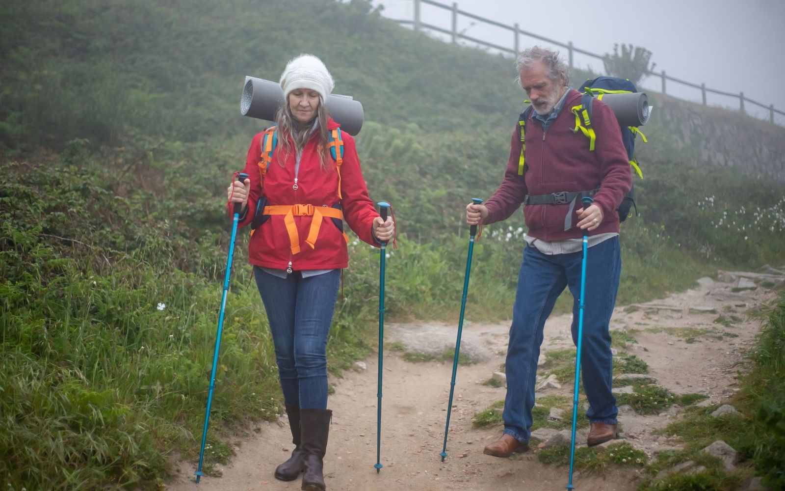 A couple with backpacks and trekking poles hiking a foggy trail.