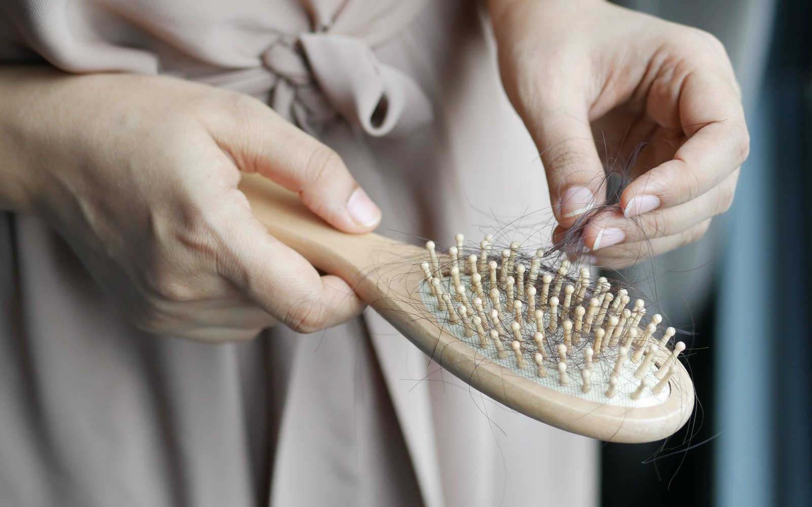 One hand holds a wooden hairbrush while the other pulls shed strands of dark hair from its bristles.