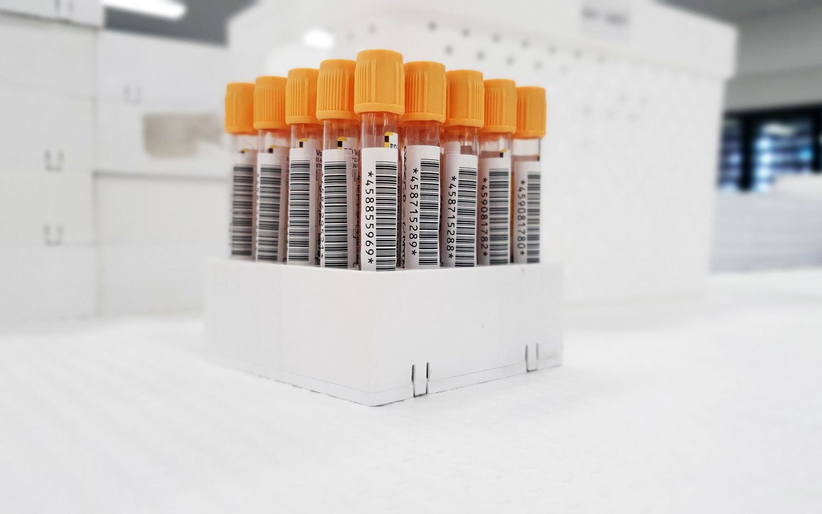 A rack of barcoded blood-sample tubes with orange caps in a laboratory.