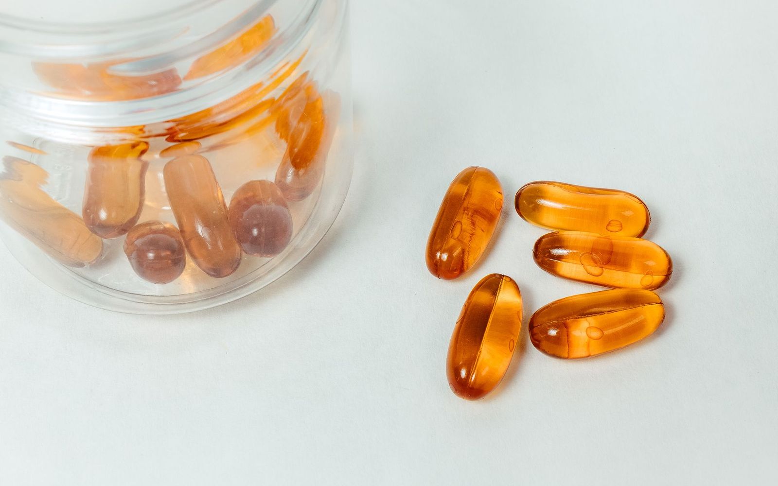 Amber softgel capsules spilling from a glass jar onto a white surface.